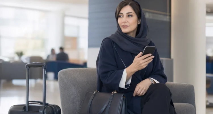 کوچ ایرانی در سفر کاری در لابی هتل با موبایل و کیف دستی، در حال مدیریت حرفه‌ای رزرو جلسات