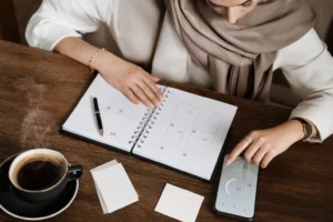 کلوزآپ نمای از بالا از دست‌های کوچ حرفه‌ای کنار دفترچه، قهوه و موبایل برای برنامه‌ریزی رزرو جلسات